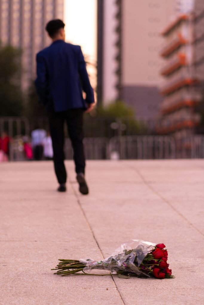 a man walking on a sidewalk with a bouquet of roses left on the pavement because the guy is on his path to learn how to get over unrequited love