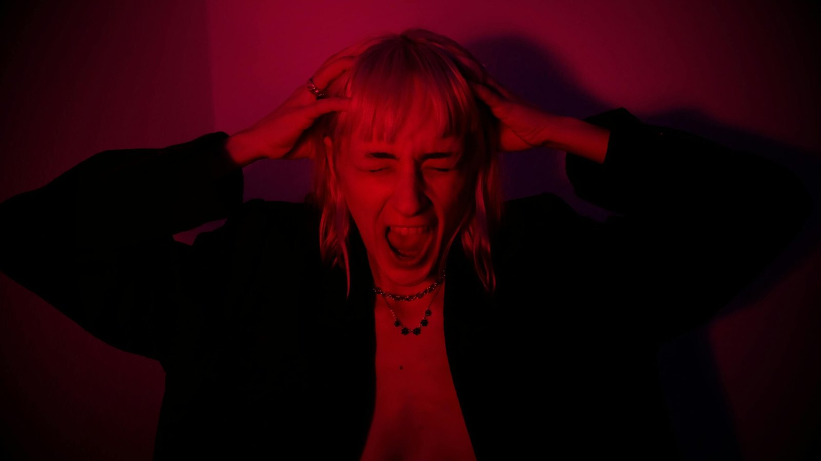 a woman in a dark red room holding her arms around her head because she is crying and managing emotional breakdown crying